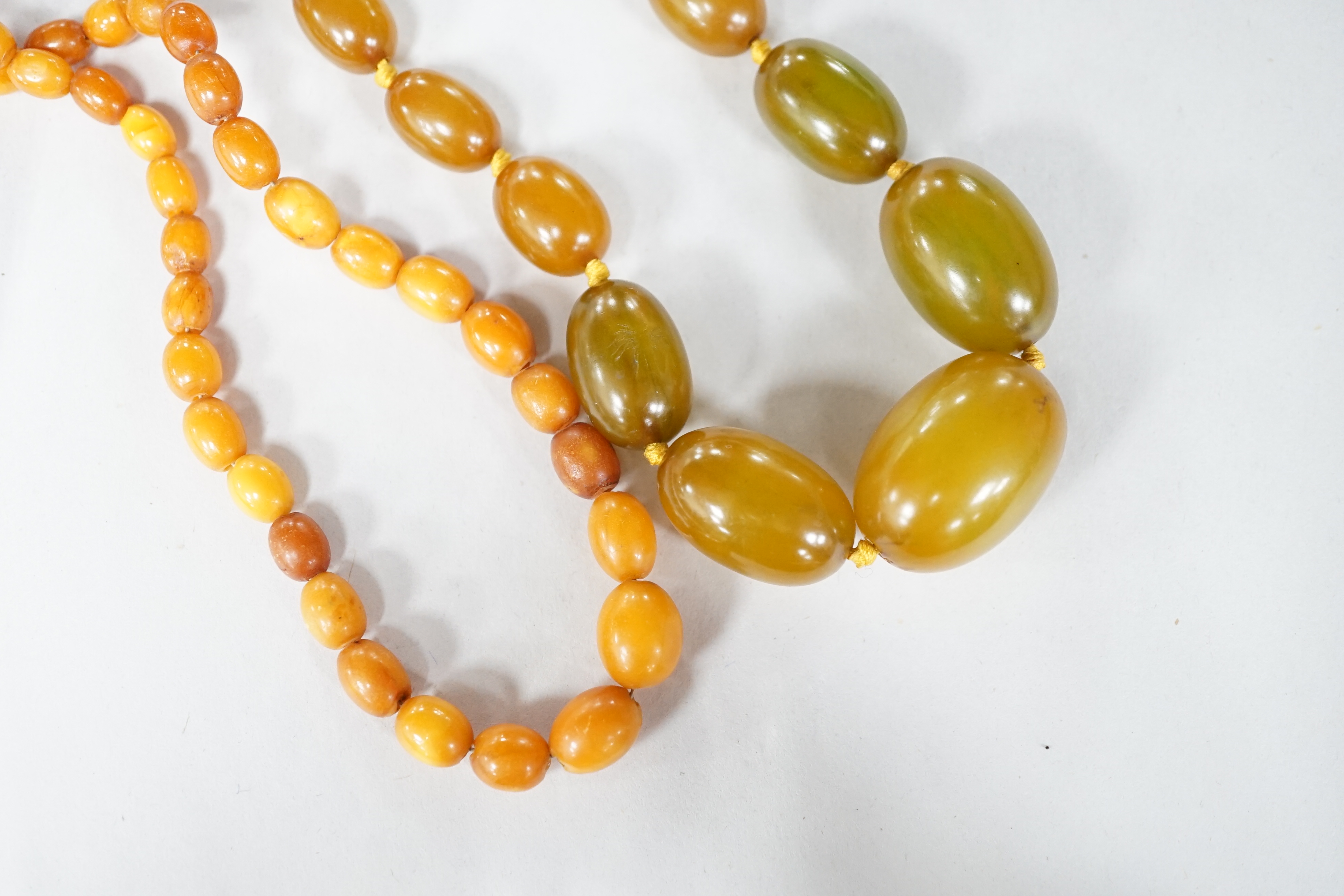 A small single strand graduated oval amber bead necklace, 40cm, gross weight 13 grams, together with a single strand graduated simulated green amber oval bead necklace, 54cm, gross weight 55 grams. Condition - poor to fa